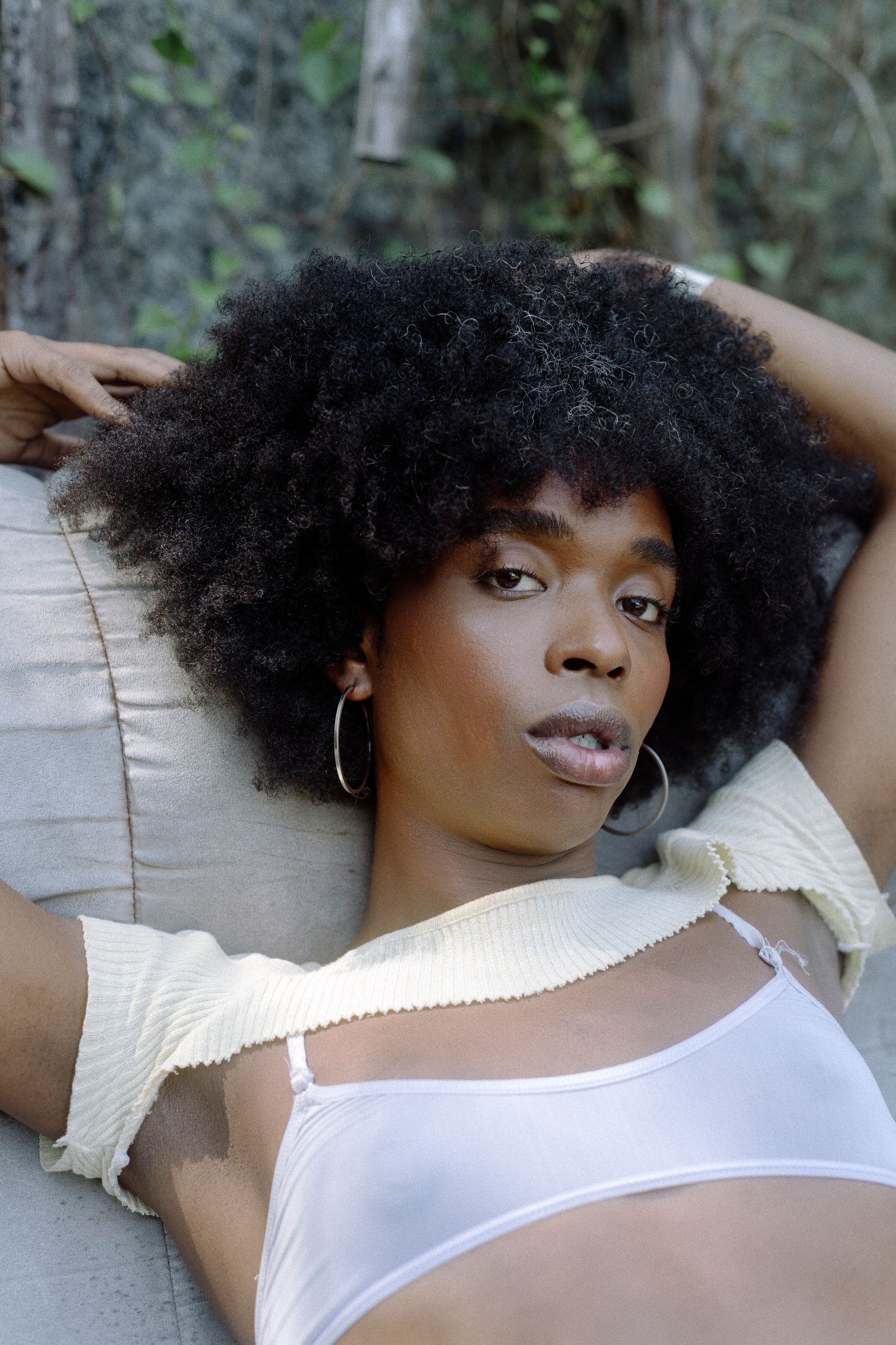 Brazilian woman named Azula laying on couch with natural hair, hoop earrings, and a two-piece crop top (photography by Rodrigo Oliveria)