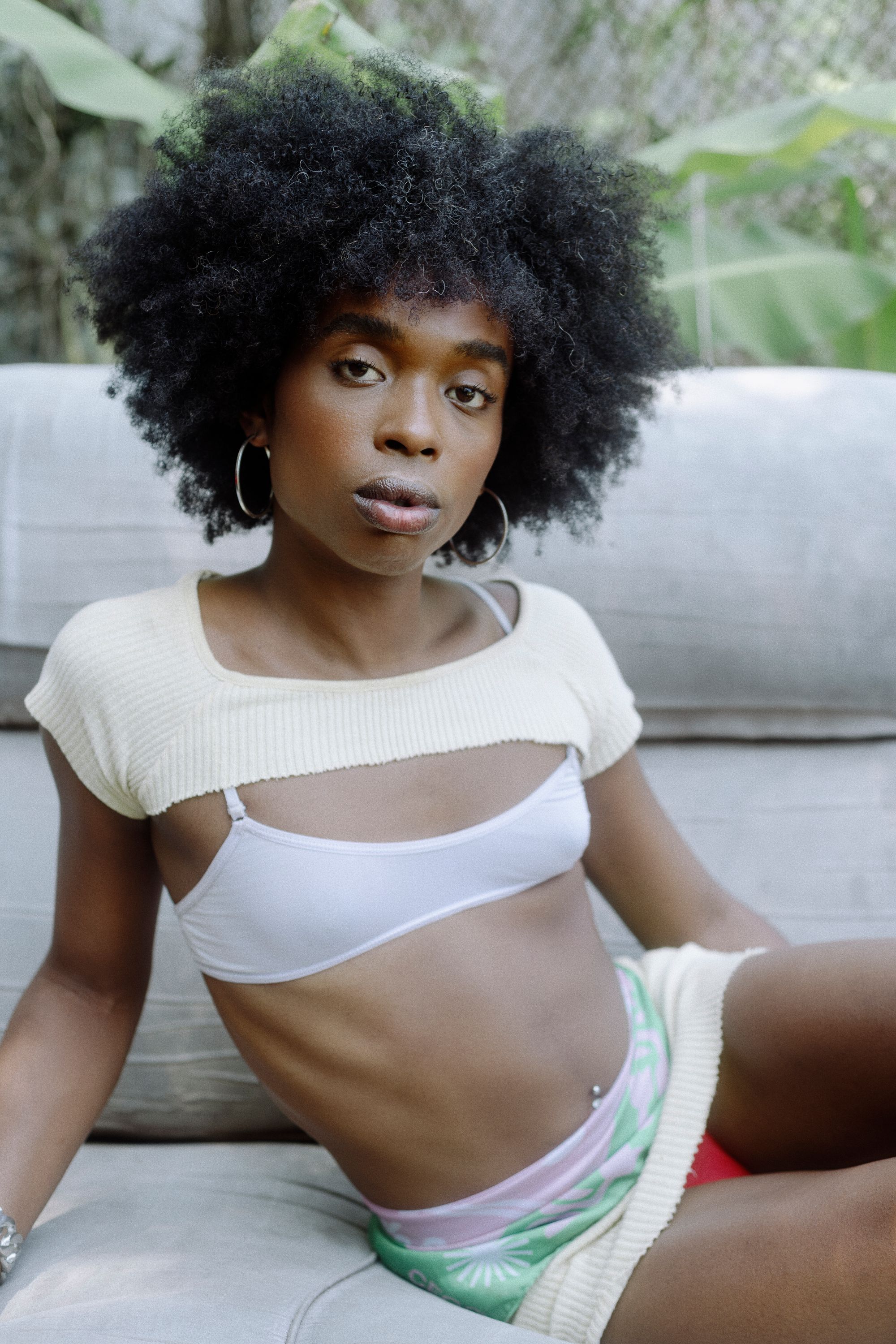 Brazilian woman named Azula laying on couch with natural hair, hoop earrings, and a two-piece crop top (photography by Rodrigo Oliveria)