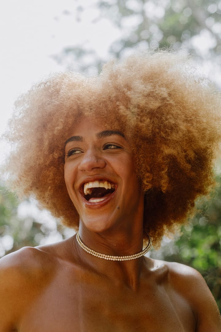 Brasilian travesti with natural red hair, wearing a crystal necklace, is smiling